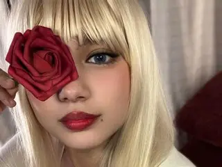 GlamourRose777 poses with a red rose held against her face, showing her blonde hair with blunt bangs and blue eyes.