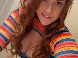 GoddessMcadams poses close-up, showing her long wavy red hair and cleavage while wearing a colorful striped top.