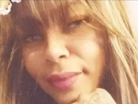 Smiling blonde woman with bangs in a soft, sunlit outdoor setting.