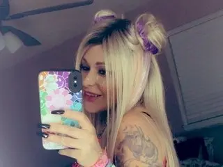 Goddesshotlips takes a mirror selfie, smiling with her long blonde hair styled in two high buns.