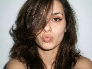 GoldenAura55 pouts her lips at the camera with messy brown hair covering part of her face.