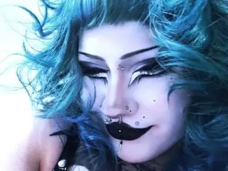 GothicLuna poses with a close-up shot, showing her blue hair, heavy dark eye makeup, and black lipstick.