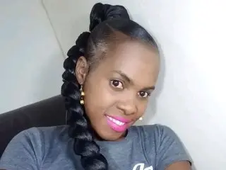 Hairrybush smiles while looking at the camera, wearing a grey t-shirt with her dark hair styled in long, thick braids.