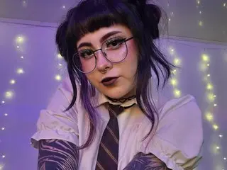 Hallucigenia wears glasses and a white collared shirt with a dark tie, posing in front of twinkling fairy lights.