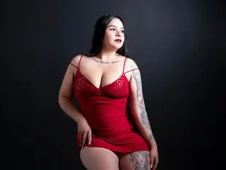 HanahMiler poses in a red lace bodysuit, showing her cleavage and tattoos against a dark background.