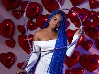Hanna_Hall poses with her long blue hair, wearing a white off-the-shoulder top while posing against a red background.