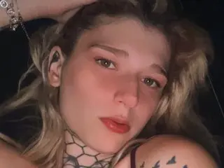 HarleyHale poses with her blonde hair messy and her hand behind her head, showing off her tattoos and makeup.