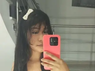 Young woman with a white hair clip taking a selfie in a modern minimalist room.
