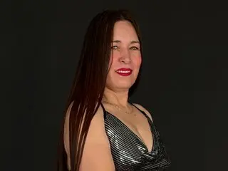 HelenLarkin poses with long dark hair and red lipstick, wearing a low-cut silver metallic top against a black background.