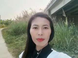 Serene portrait of a woman in a black and white blouse standing by tall grass near an overpass.