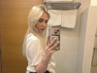 Hollyannee poses for a mirror selfie, showing her blonde hair and white top while holding her phone.