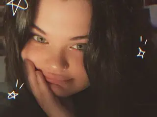 HoneyBabyxo shows her face and long dark hair, resting her chin on her hand in a close-up shot.