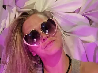 HoneyWolfxoxo poses with heart-shaped sunglasses and long blonde hair against a soft pink background.