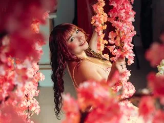 HonnyBlaice smiles while posing behind pink cherry blossom flowers in a light bikini.