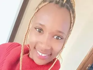 Smiling young woman with blonde braids wearing a cozy red sweater in a bright indoor setting.
