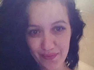 HotHoneyHot smiles at the camera, showing her face and dark, wavy hair in a close-up shot.