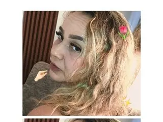 Hunty_milf poses for a close-up selfie, looking at the camera with her blonde wavy hair decorated with a small pink flower clip.