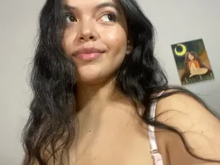 Ibizaa poses with her long dark hair down, showing her bare shoulders and chest against a plain wall.