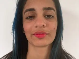 Ikarulove looks into the camera with a slight smile, showing her dark hair with blue highlights and pink lipstick.