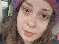 InnocentGirly looks at the camera with long brown hair and a colorful knit hat, showing her face and shoulders in a close-up shot.