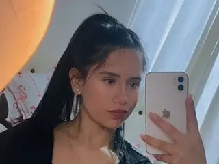 Young woman with long dark hair taking a moody selfie in a bedroom setting.
