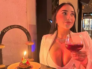 Iris_Evanss poses in a white top while holding a glass of red wine in a dimly lit room.
