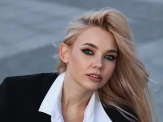 IrishWhiskey poses with a direct gaze, wearing a white collared shirt under a black blazer with her blonde hair styled down.