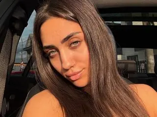 Young woman with long brown hair smiling in a sunlit car during golden hour.