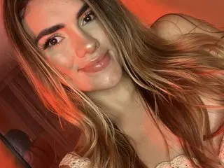 IsabellaStevens smiles while posing close-up, showing her long brown hair and light makeup in warm lighting.