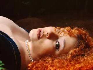IsadiaRousso poses with her red curly hair spread out, showing her face and bare shoulders against a dark background.