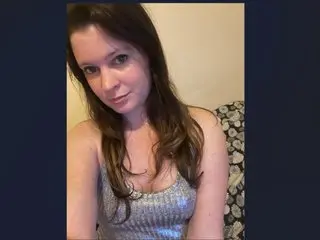 Issamayy poses with long brown hair, wearing a silver glittery top while looking directly at the camera.