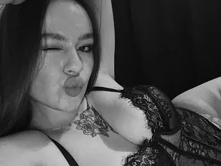 ItsSonya poses with a puckered lip, showing her cleavage in a black lace bra against a dark background.
