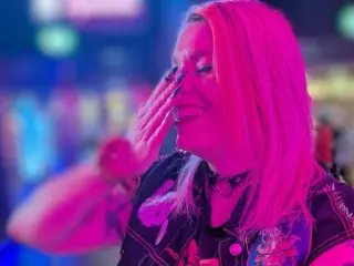 Its_Isabellaa smiles and touches her face with her hand under bright pink neon lights.