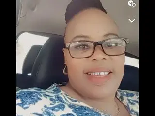Itumets smiles wearing glasses and a blue and white patterned top, showing her face and shoulders in a close-up shot.