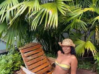 Smiling woman in a yellow bikini and straw hat relaxing in a lush tropical garden setting.