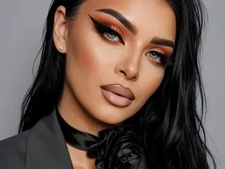 Woman with glamorous warm eyeshadow and nude lip makeup wearing a black blazer and floral neck accessory.