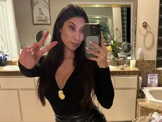 Ivoryftxo poses in a black top with long dark hair, looking into a mirror in a bathroom setting.