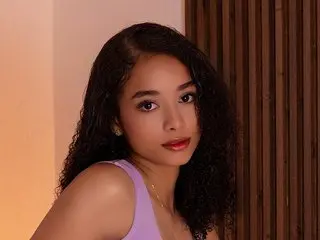 Young woman with curly dark hair wearing a lavender top in a warm, moody indoor setting.