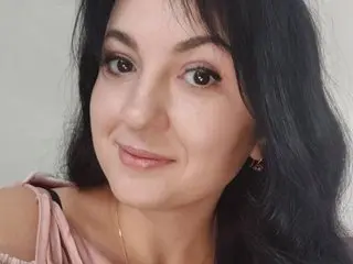 Smiling woman with long dark hair wearing a pink top in a bright indoor setting.