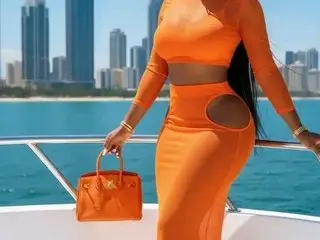 JELLYASS23XX poses in an orange long-sleeve crop top and matching skirt against a blue ocean and city skyline background.