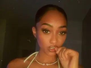 JadeDillin poses with her hand near her mouth, showing her face, dark hair, and a silver necklace against a dark background.