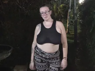 Smiling woman in a black sports bra and patterned bohemian pants standing in a lush tropical garden at night.