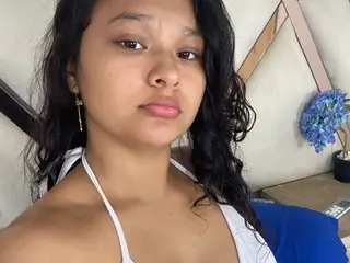 Jade_ht poses close-up, showing her face and shoulders with long, dark wavy hair and a white tank top strap visible.