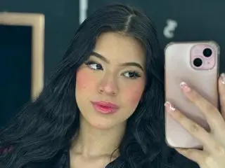 JeannaVender poses with long black hair and pink blush, looking directly at the camera in a close-up headshot.