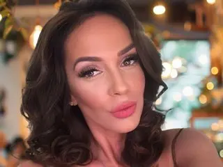 Jennifer_Hills poses with a close-up headshot, showing her long dark hair and red lipstick against a soft, blurred background.