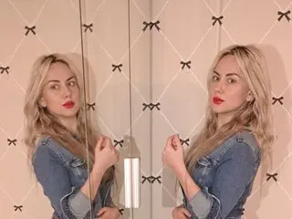 JennyJes poses in a mirror reflection, wearing a denim top and showing her blonde hair and red lipstick.