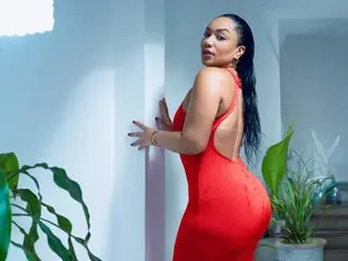 JesicaTaylor poses sideways in a tight red dress, showing her back and profile against a plain light wall.