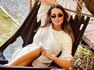 JessieBlonde poses in a white blouse while relaxing in a black hammock outdoors.