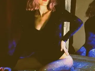 Woman in a sparkly black bodysuit and sheer tights posing in moody, low-light indoor setting.
