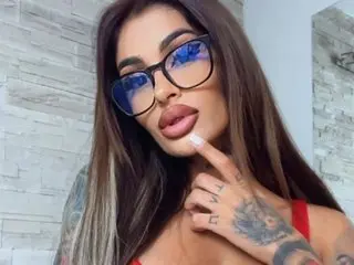 Jessy_Cruz poses with long brown hair and glasses, showing her face and shoulders while wearing a red top.